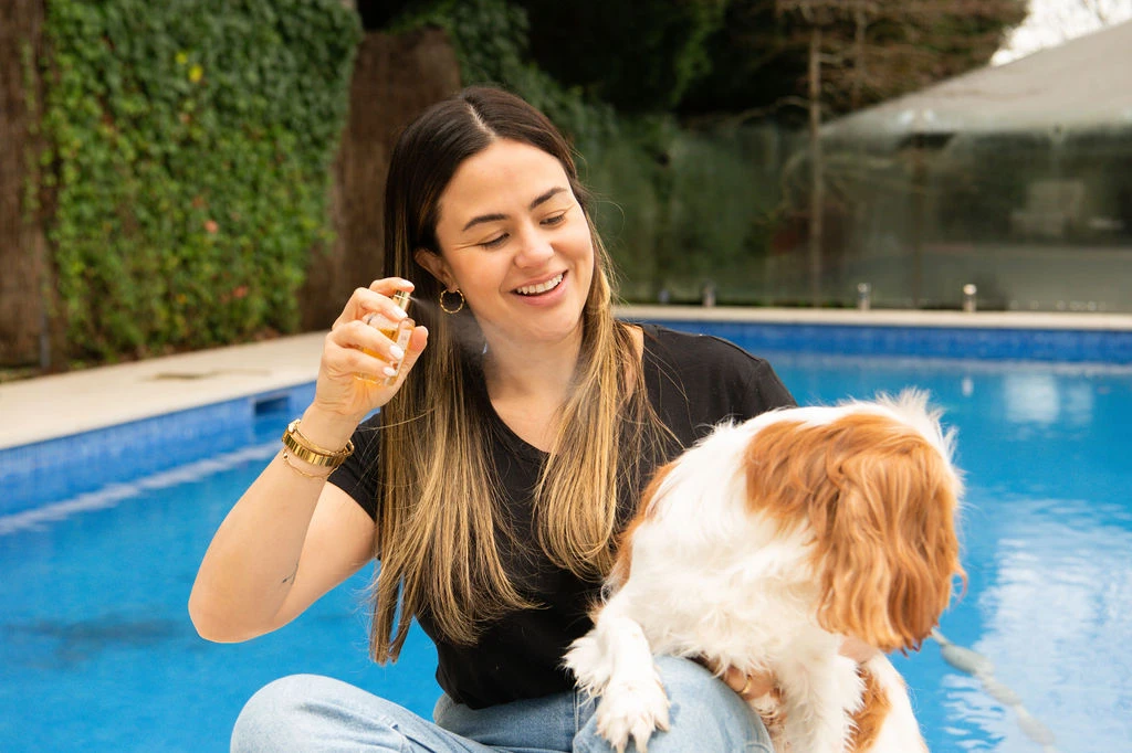 A person spraying Pa & Paws Pet Perfume near a Cavalier King Charles Spaniel, poolside.